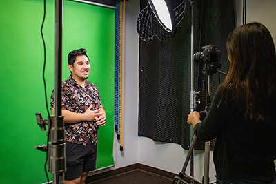 Student in front of a green screen while being filmed by another person