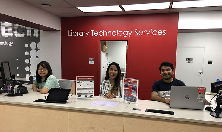 Three students sitting behind a service desk.