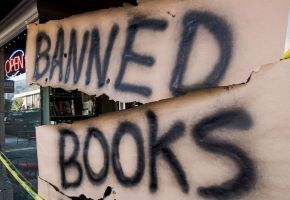 Graffiti on cardboard covers a storefront, reading "Banned Books"