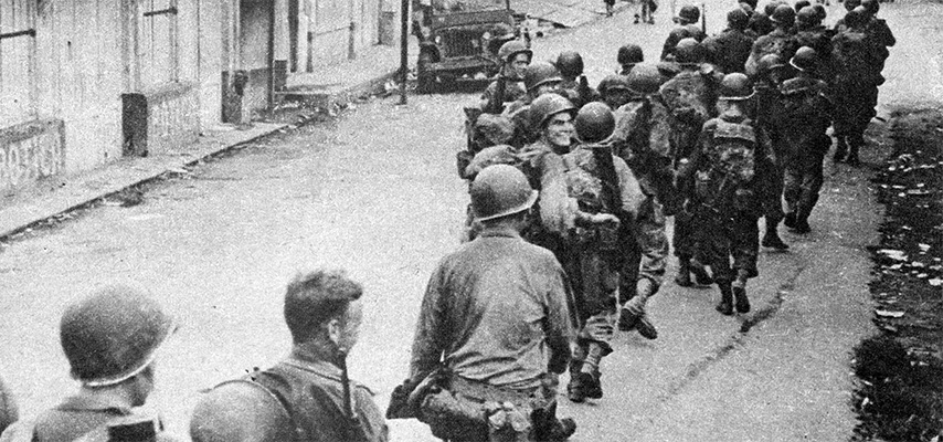 soldiers march past wooden buildings