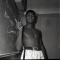 Cassius Clay, (soon to be Muhammad Ali) points to a chalk board that reads "Moore in 4, Next Champ Cassius Clay" at an event leading up to his boxing match against Archie Moore at the Sports Arena, November 15, 1962,  Harry Adams Collection. ID: 93.01.HA.B4.N120.605.1