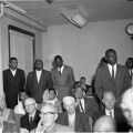 Several men in suits stand around a seated Malcolm X, Harry Adams Photograph Collection