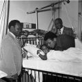 Boxer Muhammad Ali visits an unidentified young patient who is laying in a hospital bed. Two unidentified men are also visible in photo, 1972. Harry Adams Collection.  ID: 93.01.HA.N120.B27.45.187.09