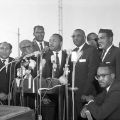 Dr. Martin Luther King, Jr., stands at a lectern. Standing with him are (from left) Juan Cornejo, the first Mexican American mayor of Crystal City, Texas; Los Angeles City Councilmen Gilbert Lindsay and Tom Bradley; and to Dr. King's right, Dr. C. Albert Henson, president of the Baptist Ministers Conference of Los Angeles and Southern California. Freedom Rally, 1963 May 26, Harry Adams Collection, 93.01.HA.B6.N45.953