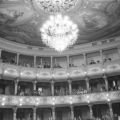 Interior of opera house, with audience in balcony levels, with chandelier and ornate ceiling at top
