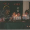 A traditional Brownie candle lighting ceremony is shown with the troop leader leaning into the picture, 1995
