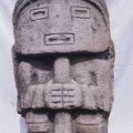 Stone statue of a figure with a mask-like face and holding a staff stands at the Ullumbe site in San Agustín Archaeological Park. Photo taken in 1975. Digital ID: 99.01.RCr.sl.B17.04.28.05