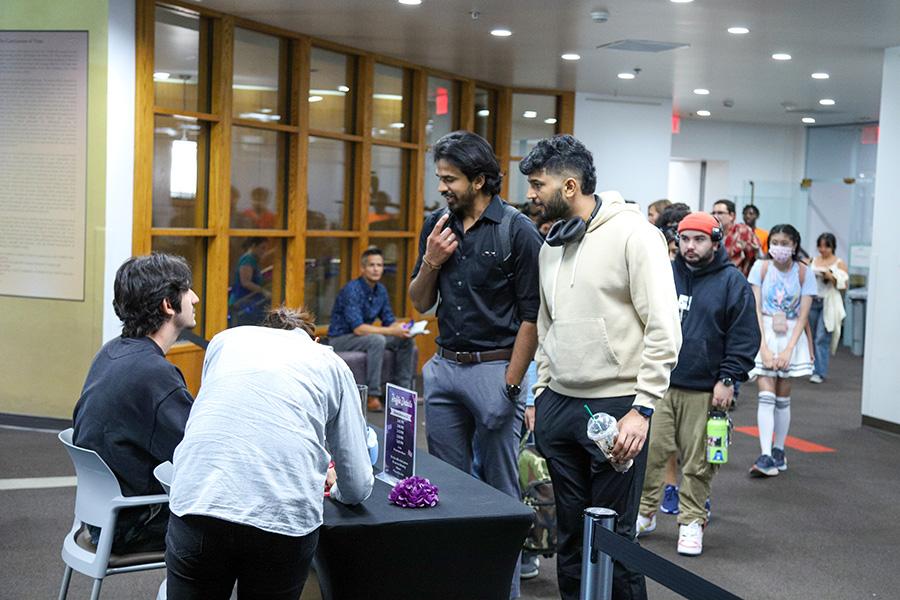 Two students talking to someone at a desk