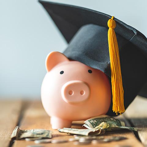 A piggy bank wearing a graduation cap with money around it
