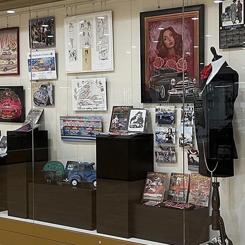 Display case at the Politics of Low & Slow Exhibition, posters, suits, magazines, model cars