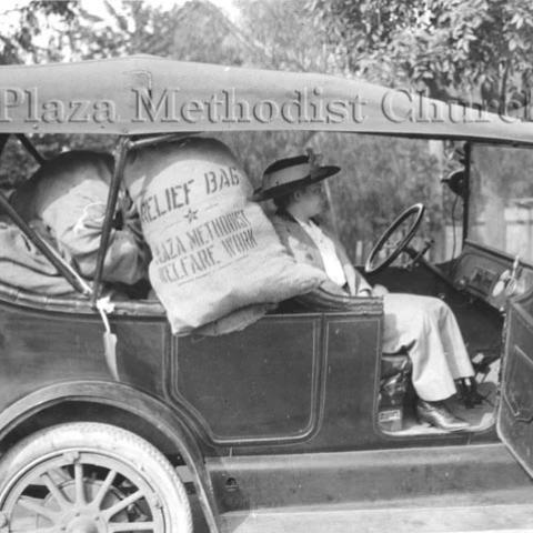 A woman sitting in an old car filled with goods