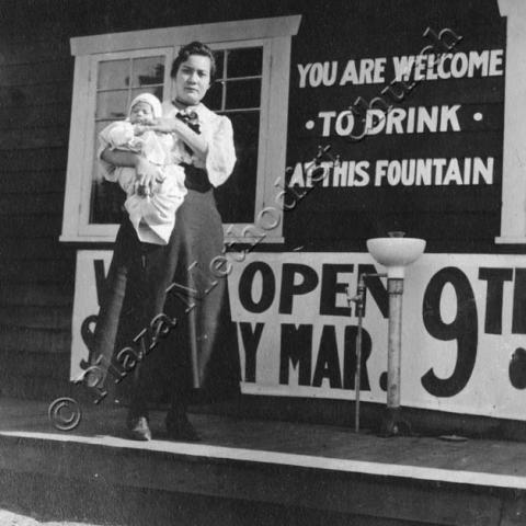 A woman standing holding her infant child next to a water fountain