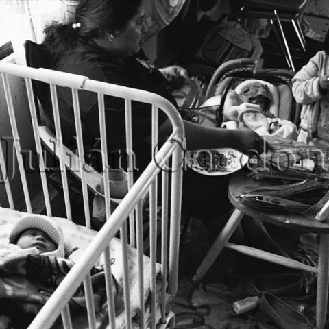 A baby in a cradle and a woman sitting next to it taking care of other children.