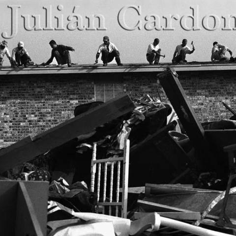 Men with hammers working on fixing the roof of a building next to a pile of debris.