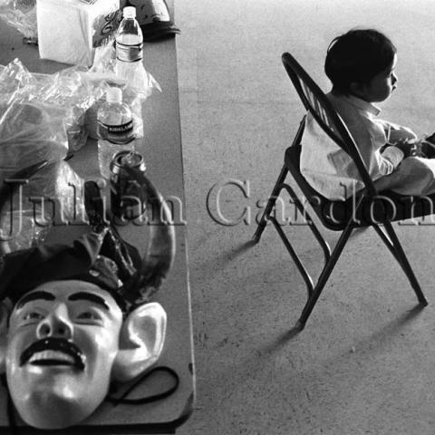 Devil masks, water bottles placed on a table and a child sitting on a chair next to it.