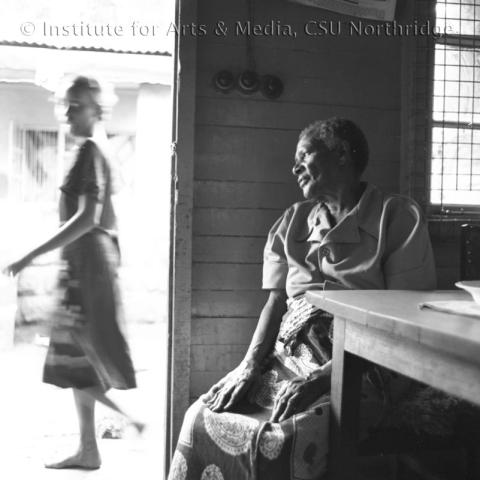 A person sitting inside the house and a person walking outside the main door.