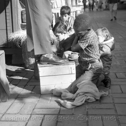 Children polishing shoes on top of a wooden basket