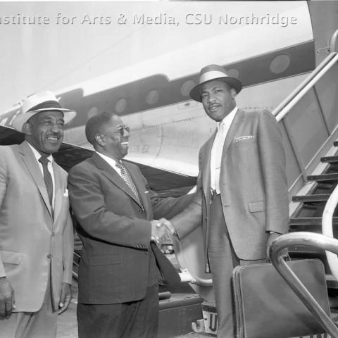 Martin Luther King shaking hands with a man in front of an airplane.