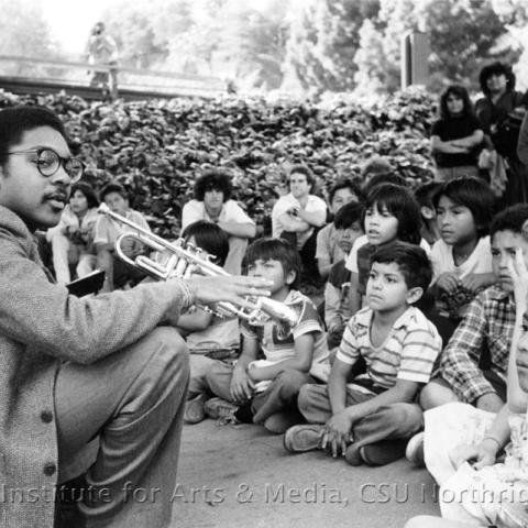 children seated while a man holds his trumpet.