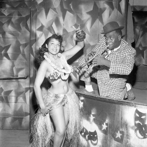 A woman dancing wearing a lei and a man playing the trumpet.