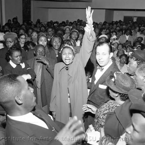 A woman standing out with her arm up in the middle of a crowded room.