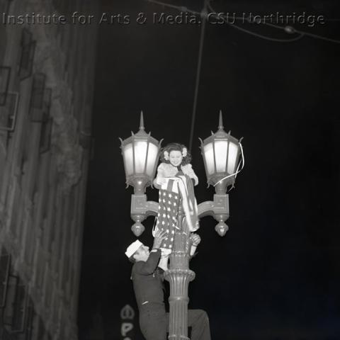 Woman standing on top of a light pole with man holding her.