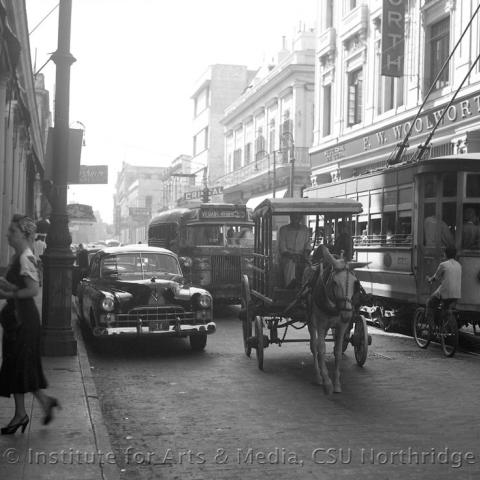 A busy street with cars buses and horse carts.