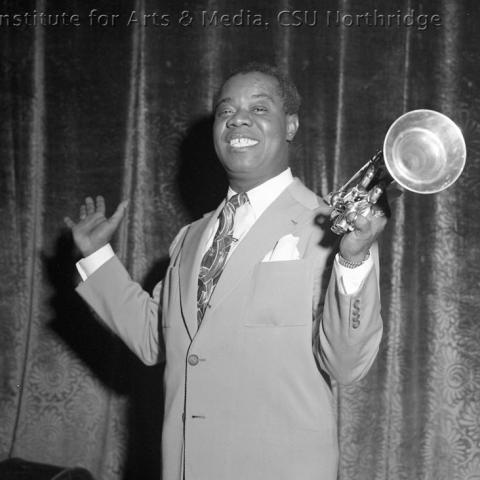 A man in a suit posing with a trumpet.