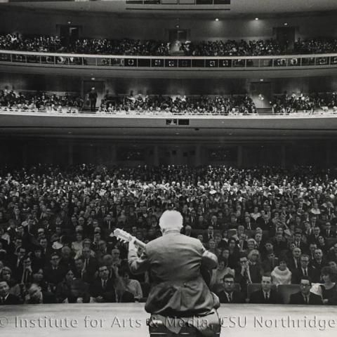 Man playing guitar on stage and audience watching.