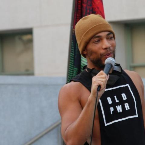 A man wearing BLD PWR t shirts speaks on a microphone.