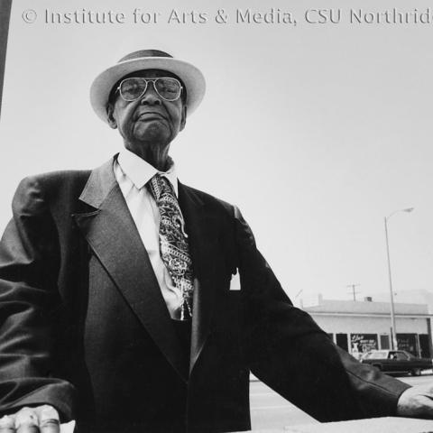 An elderly man in a suit and a hat on.