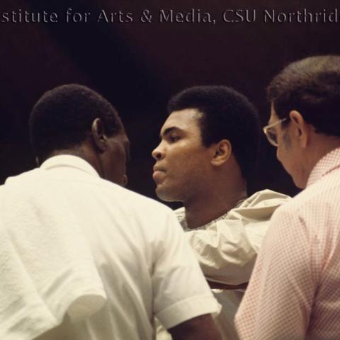 Muhammed Ali at the corner of a boxing ring with cornermen.