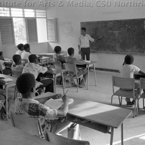 A classroom with kids and teacher pointing at the blackboard. 