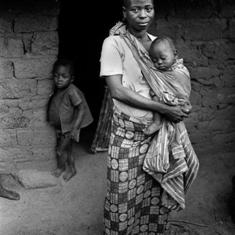 A woman carrying her infant child with a cloth wrapped around her shoulder.