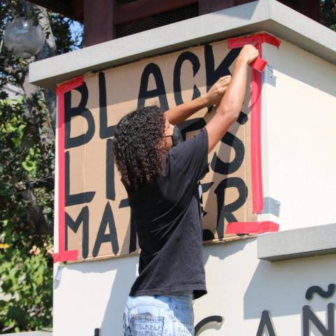 A person taping a black lives matter board on a wall.