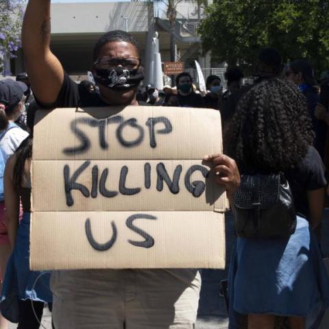 A black person holding a board that says stop killing us.