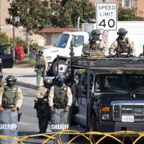 Officials block the road with razor wire and stand with shields.