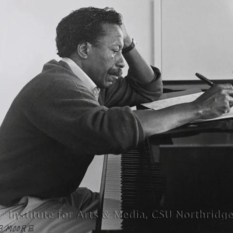 A man writing on a book placed on a piano.