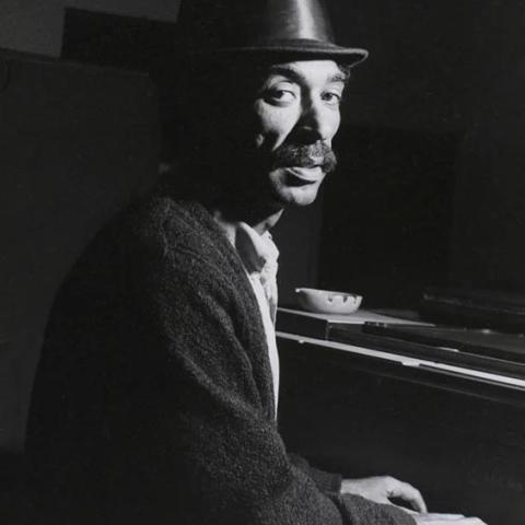 A man playing a piano with a hat on.