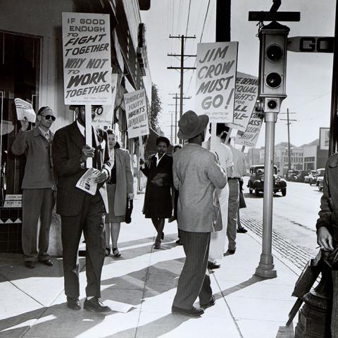 Men marching with picket signs that read IF GOOD ENOUGH TO FIGHT TOGETHER WHY NOT TO WORK TOGETHER and JIM CROW MUST GO!