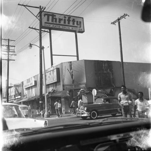 Watts Central Avenue; view of Thrifty's Drug Store, men standing around, and two young men carrying items, 1965, Charles Williams Collection, Tom & Ethel Bradley Center Photographs
