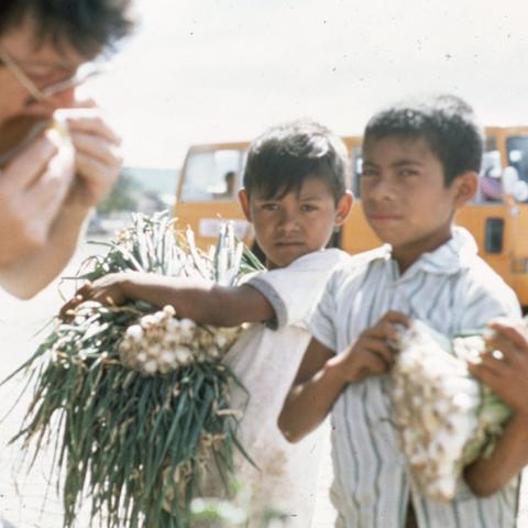 Two young boys carrying produce to adjacent Mike Emery at the Pan-American Highway in Nicaragua, on the way to Esteli, a Sandidista stronghold. ca. 1986-1988. Box 3, Folder 1