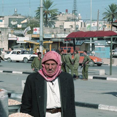 A Palestinian shopkeeper posing for the camera with Israeli Defense Force soldiers behind him, in Gaza. 1989. Box 6, Folder 6.