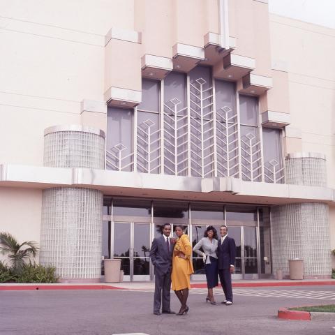 Two well dressed couples, stand and pose in front of the entrance of the Baldwin Hills Crenshaw Plaza for a brochure advertising the mall’s offerings taken by Roland Charles, 1989. Roland Charles Collection, Box 21. 