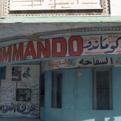 An abandoned theater in Gaza covered in posters and titles for Arnold Schwarzenegger and Sylvester Stallone films. 1989. Box 6, Folder 6. 