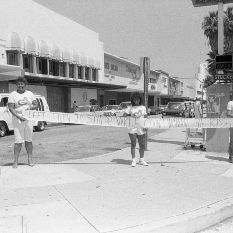 Three organizers wearing "Crenshaw! Toward a Greater Community" t-shirts standing on the corner of Stocker St. and Crenshaw holding a sign reading, "Left turn too slow?? Write Councilwoman Pat Russell," 1986. Guy Crowder Collection, 11.06.GC.N35.B11.25.37.08.