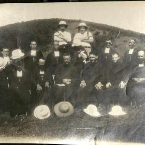 Photograph of twelve Catholic priests posing with two men brandishing pistols