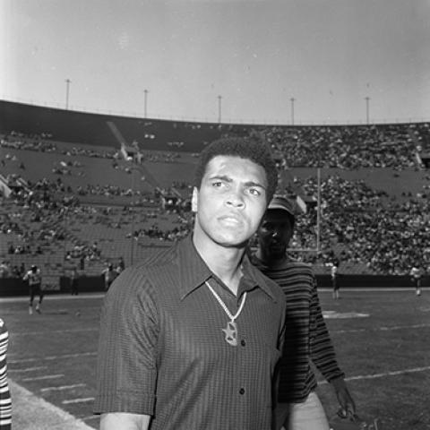 Heavyweight boxing champion and activist Muhammad Ali attends the Freedom Football Classic at Los Angeles Memorial Coliseum. Civil rights activist Willis Edwards is standing behind Ali, 1973. Harry Adams Collection. ID: 93.01.HA.N120.B25.11.51.02