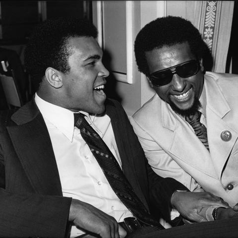 Muhammad Ali shares a laugh with Stokely Carmichael in a meeting room during a special event, 1973. Guy Crowder Collection. ID: 91.01.GC.P.B1.28