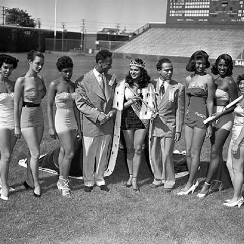 Photographer Charles Williams (fourth from left) stands next to Tina Thomas, winner of the 2nd Annual Queen of the Cavalcade of Jazz (or Sun Crest Queen) beauty contest, and her court, which included Joyce Sonnier, Delores Johnson, Carolyn Matthews, Bobbie Jones, Barbara Bartlett, and Rose-Mary Collins. Cavalcade of Jazz, 1952, Harry Adams Collection, 93.01.HA.N45.B34.152